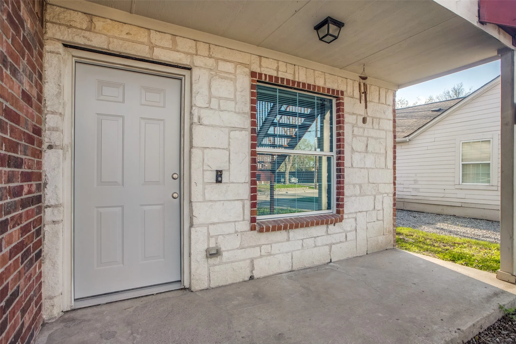 Covered porch entry featuring a paneled door, stone facade, and a window with brick trim