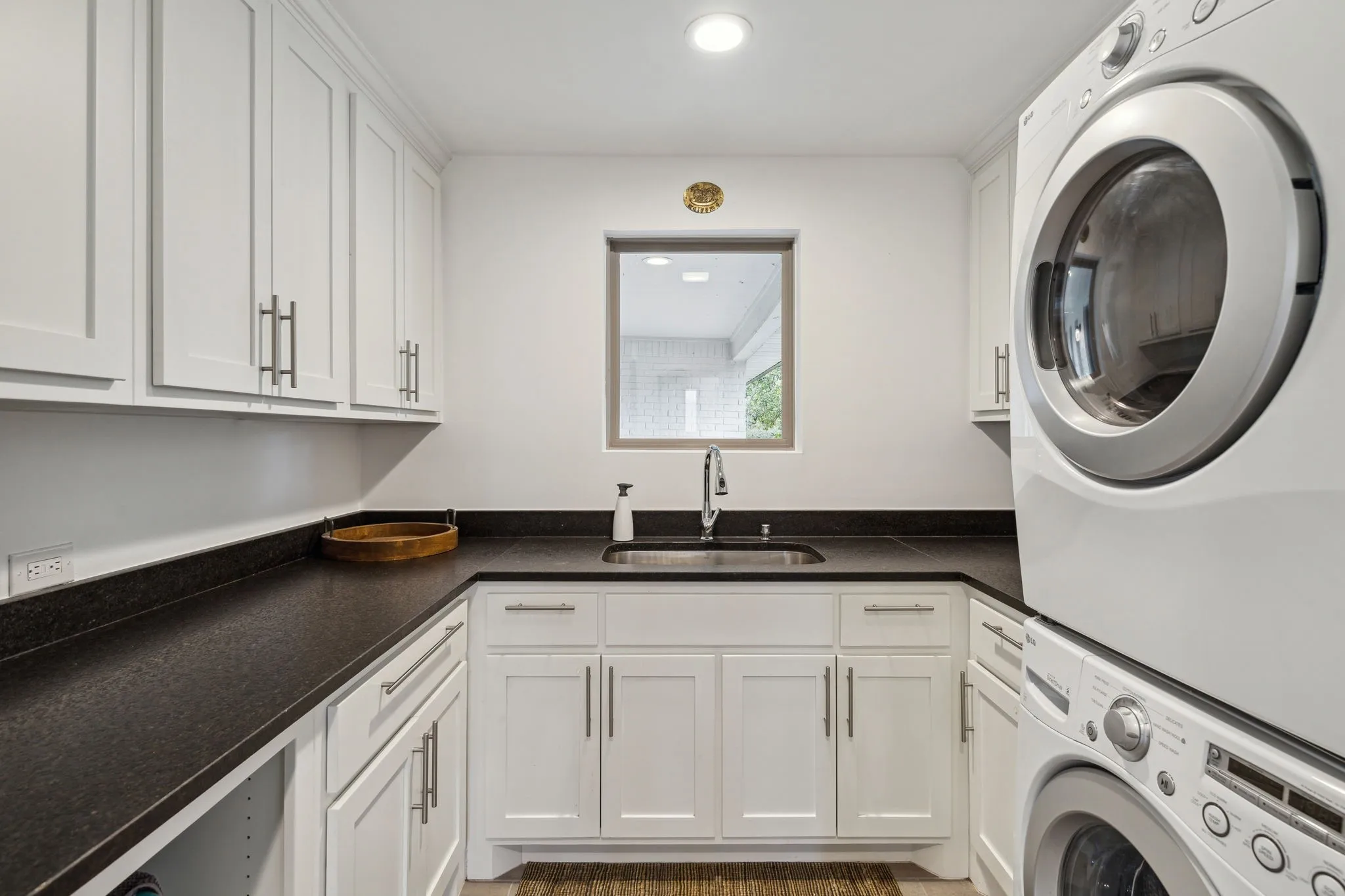 Washroom featuring stacked washer and dryer, custom cabinets, and sink