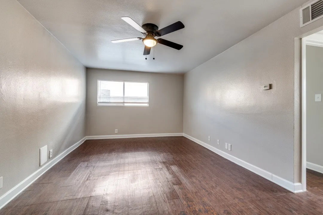 Spacious room featuring wood-finish flooring, light gray walls, a ceiling fan with integrated lighting, and a window with blinds