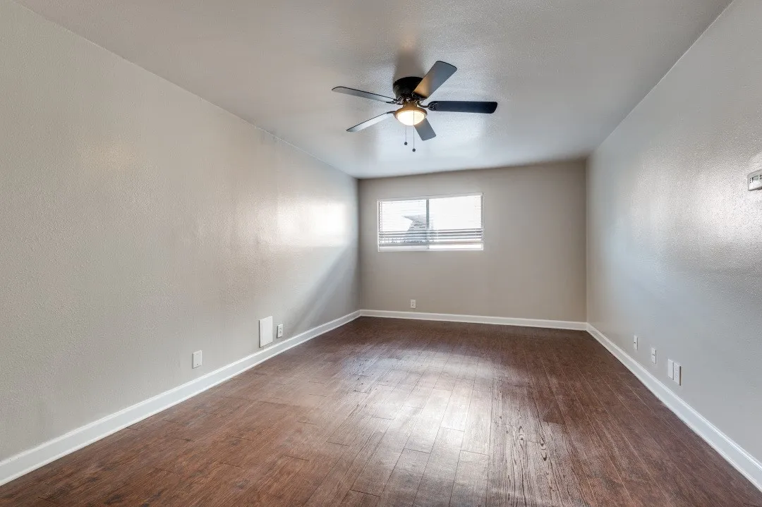 Spacious room featuring wood-finish flooring, neutral-toned walls, a ceiling fan with integrated lighting, and a window with horizontal blinds