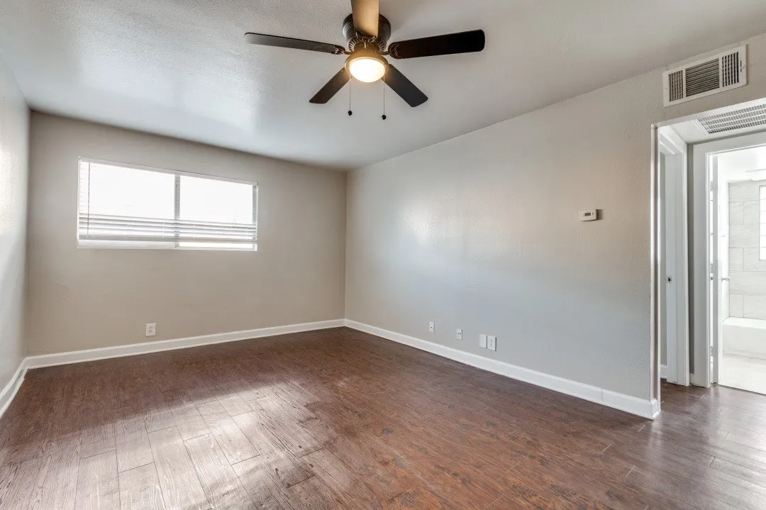 Spacious room with wood-finish flooring, a ceiling fan with integrated lighting, and a large window featuring horizontal blinds