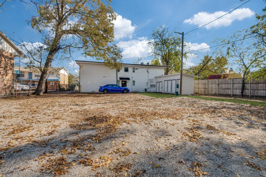 Gravel parking area featuring mature trees and a privacy fence bordering the property