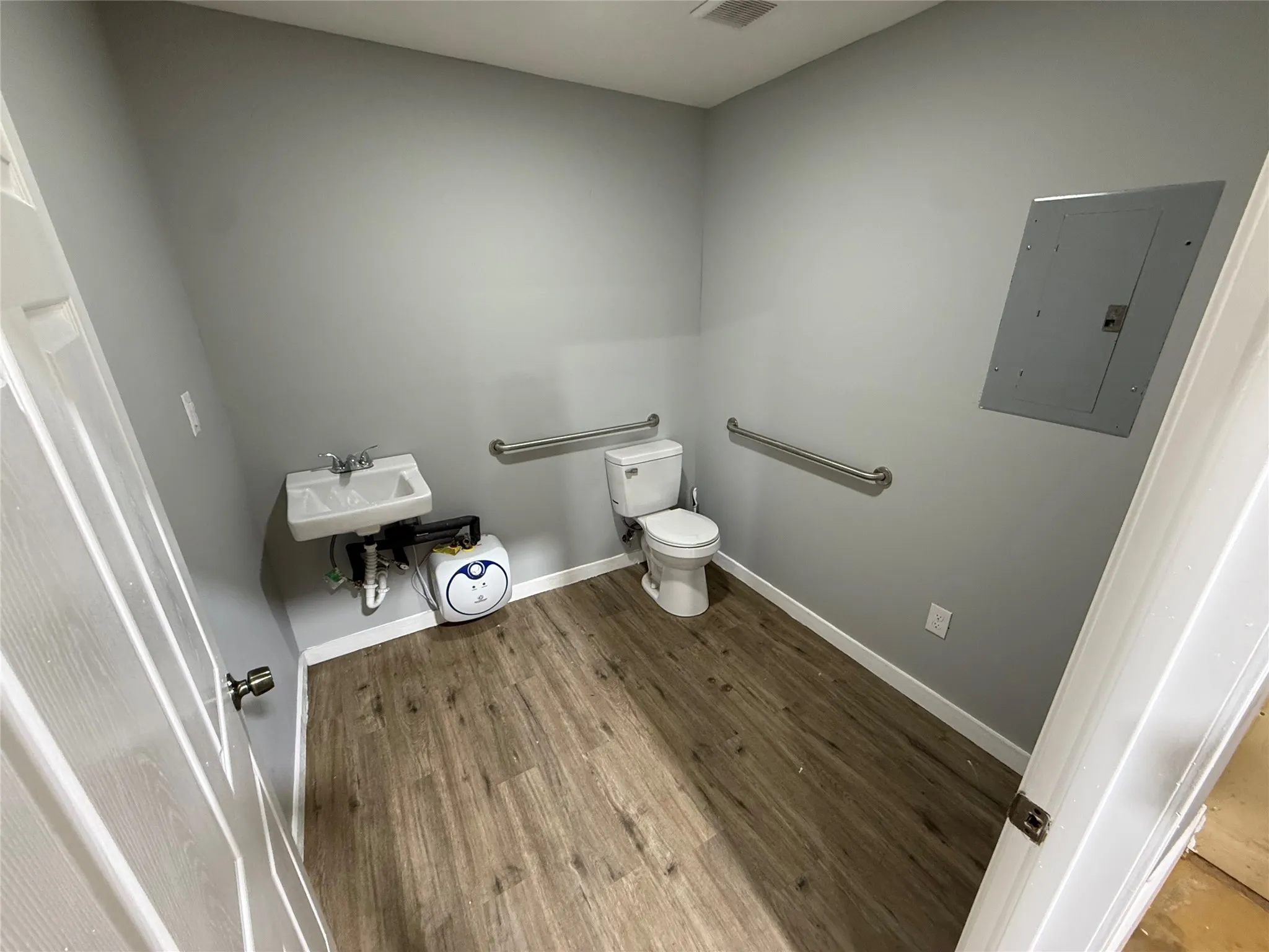 Powder room featuring a wall-mounted sink, toilet, safety grab bars, and wood-finish flooring