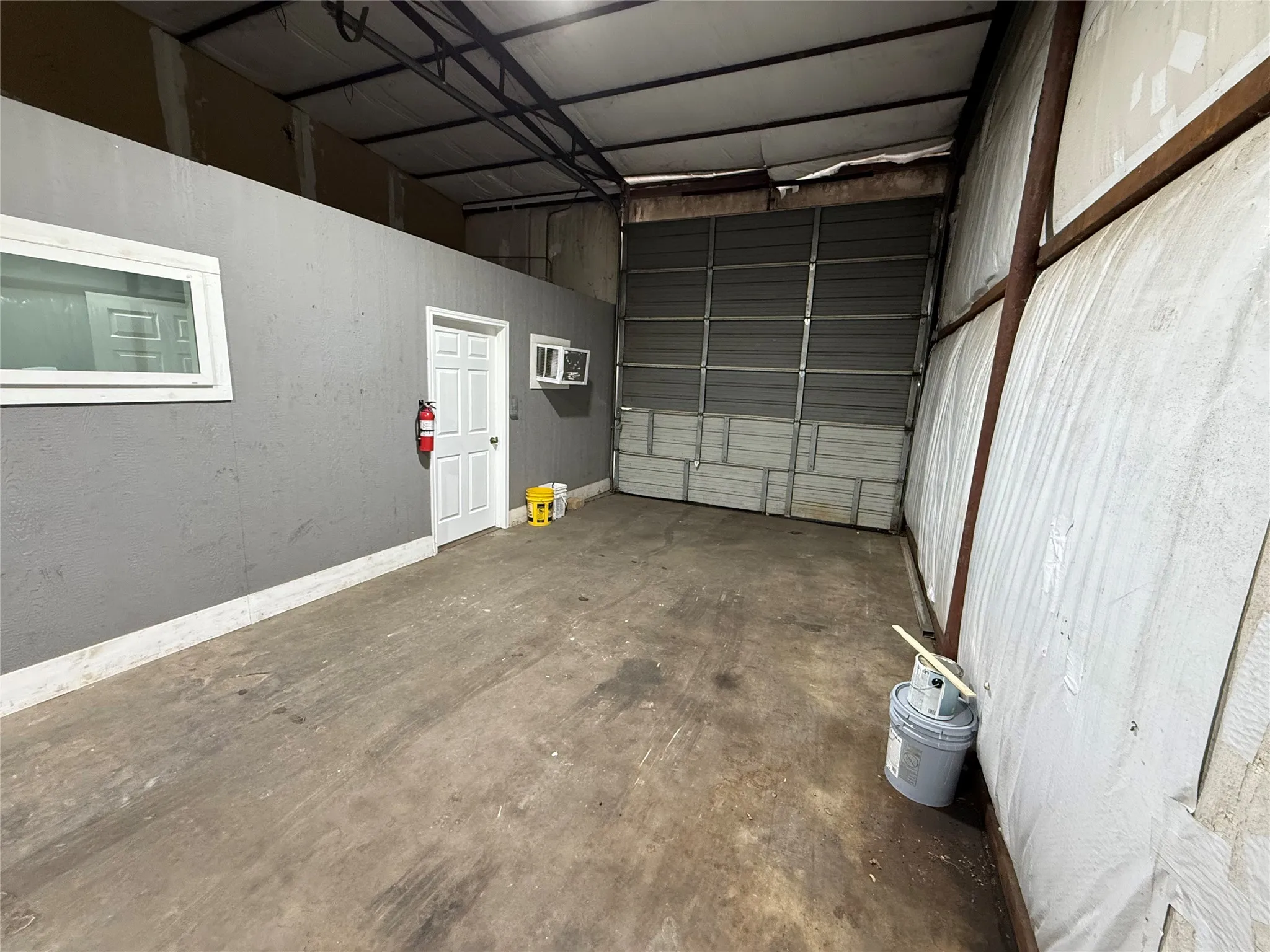 Warehouse interior featuring a concrete floor, a roll-up door, and exposed structural beams
