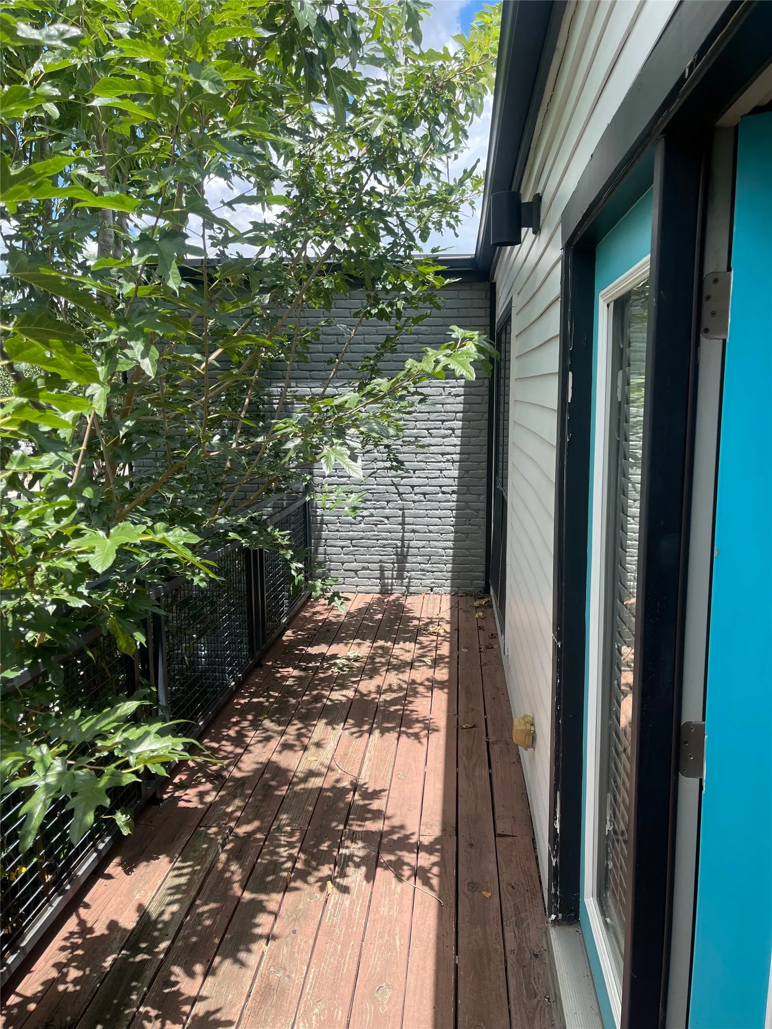 Wood-finish decking with a dark metal railing, gray brick-patterned exterior wall, and light-colored siding