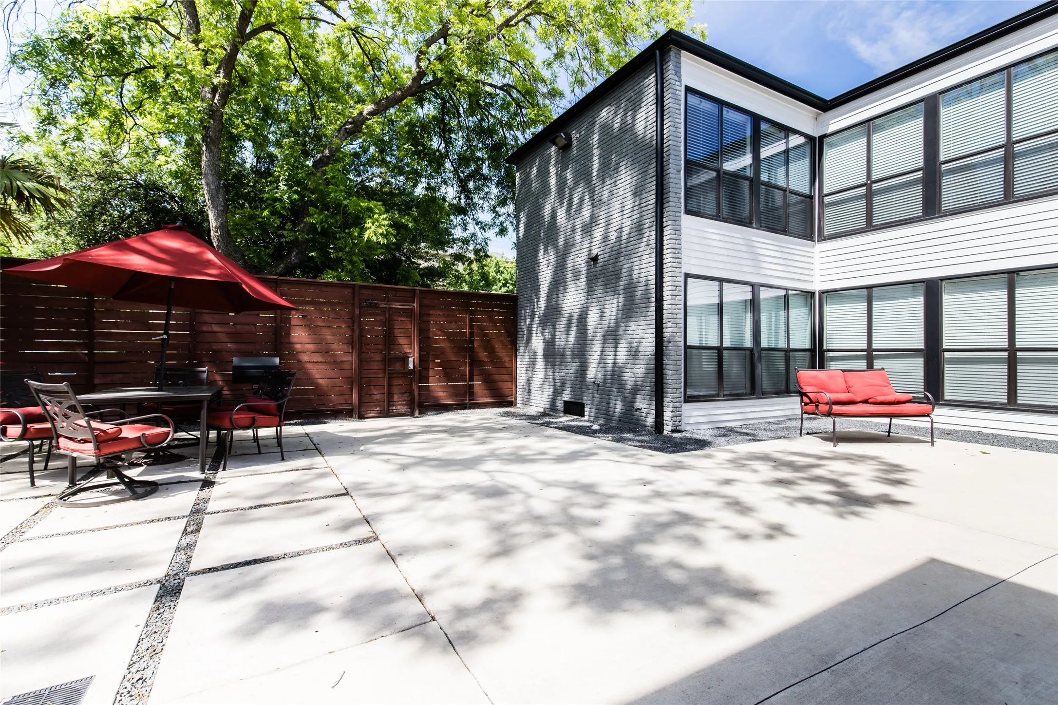 Expansive concrete patio featuring decorative stone inlays, a horizontal plank fence, and mature trees providing natural shading