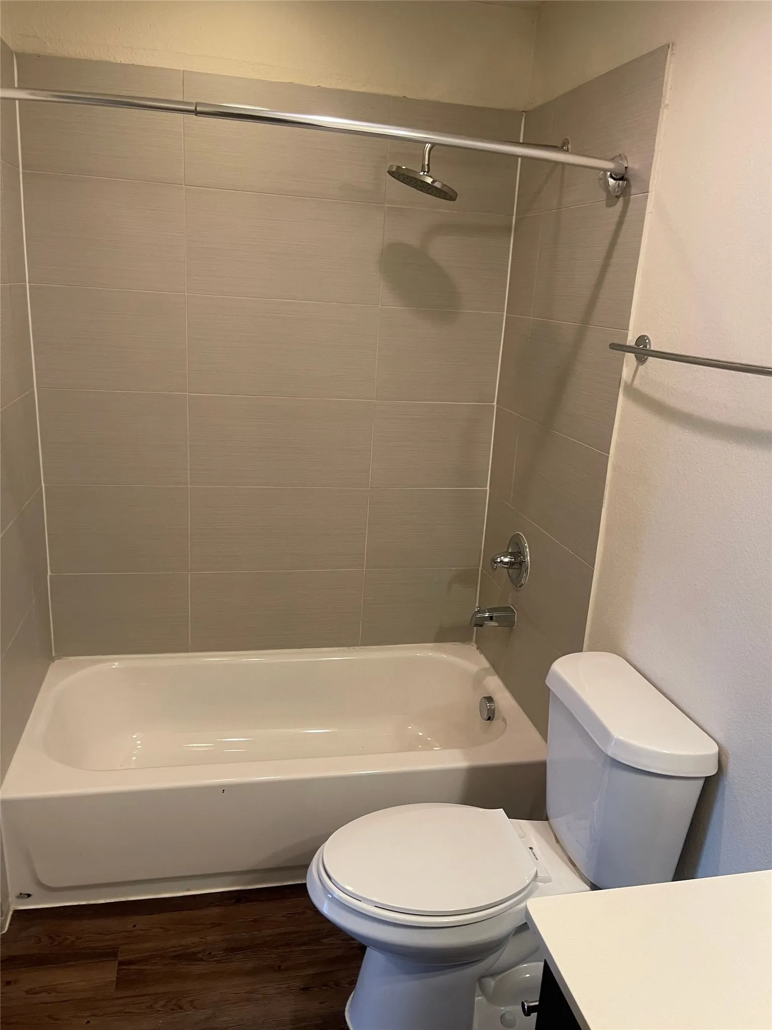 Bathroom featuring a white bathtub and toilet, light gray subway tile shower surround, chrome fixtures, and wood-finish flooring