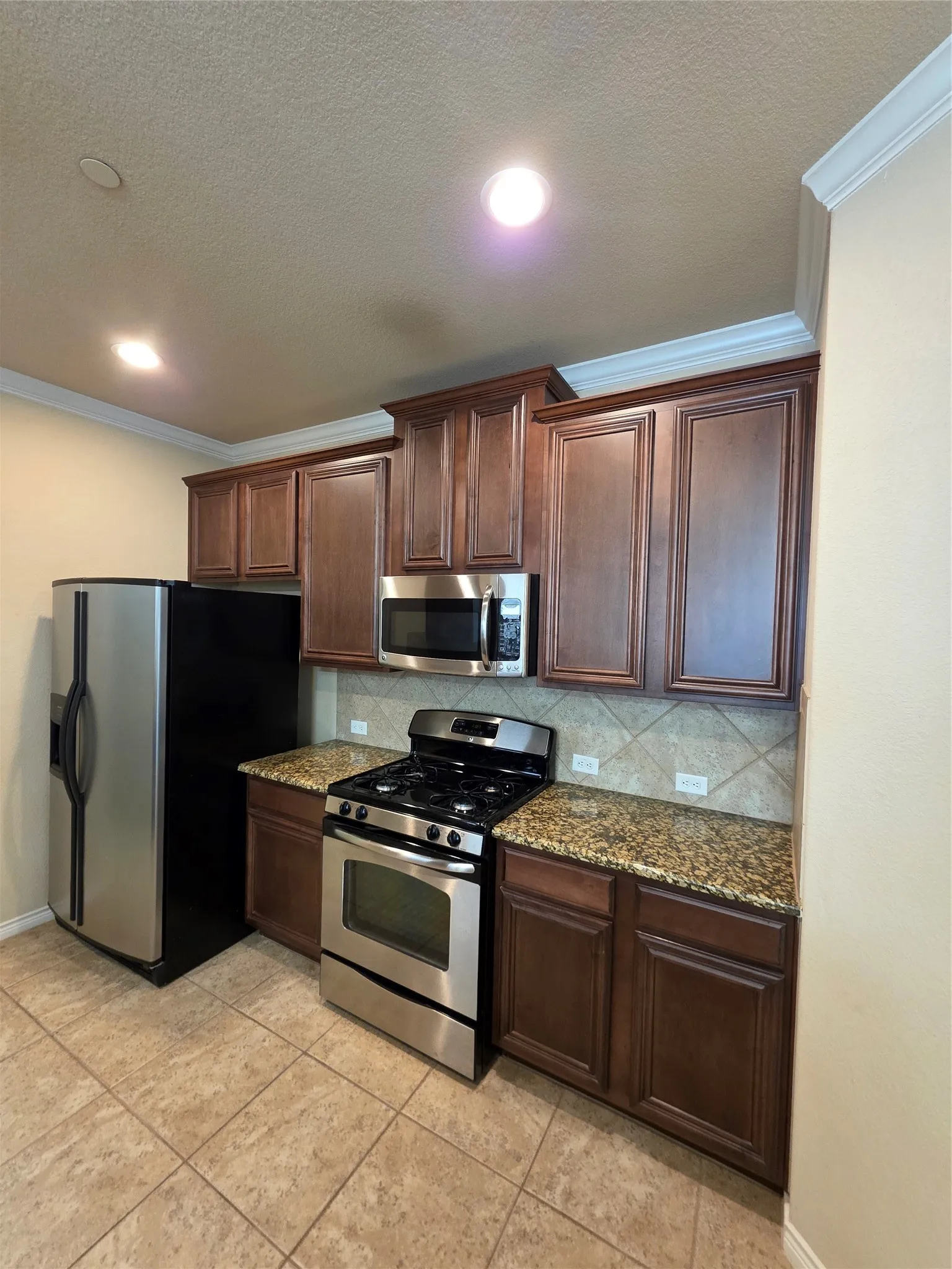 Kitchen featuring stainless steel appliances, wood-finish cabinetry, granite countertops, and tile flooring