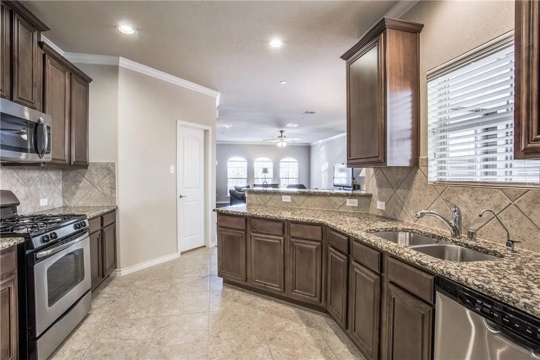 Kitchen featuring dark wood-finish cabinetry, stainless steel appliances, speckled stone countertops, and a tile backsplash