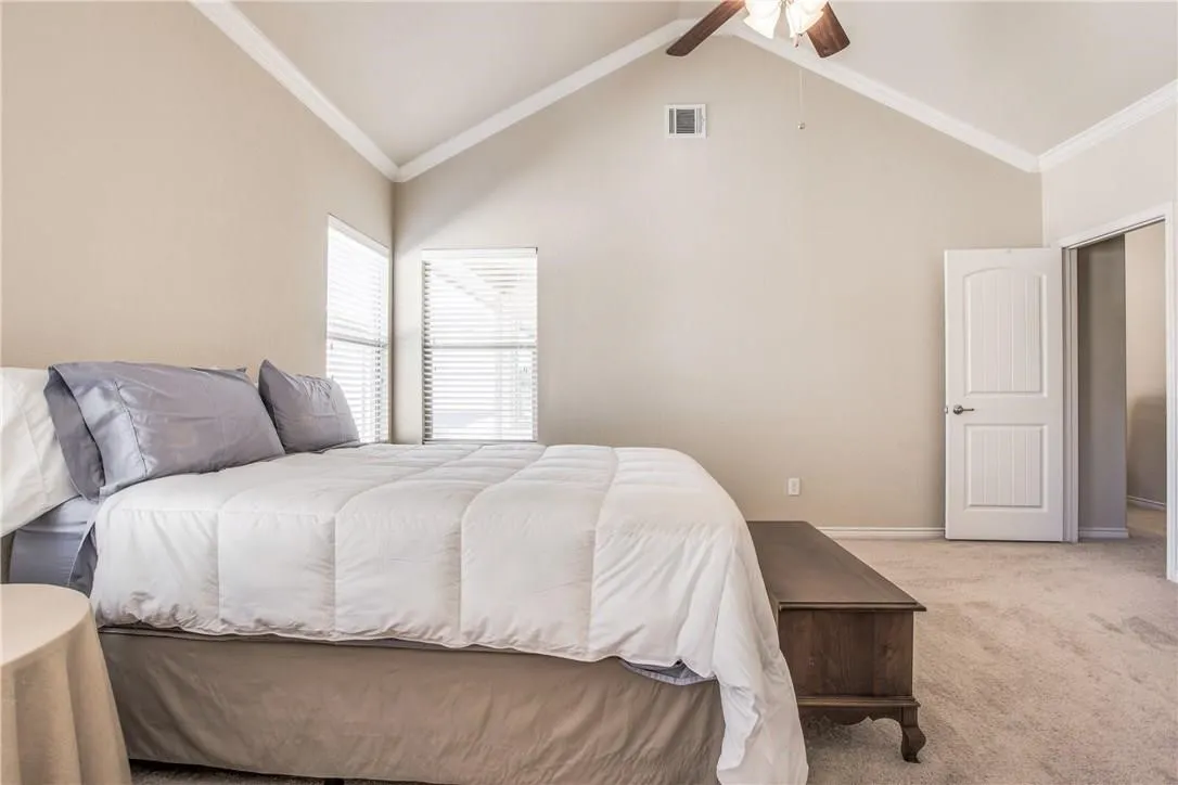 Vaulted ceiling bedroom featuring beige wall tones, two windows with blinds, a white paneled door, and light-colored carpet flooring