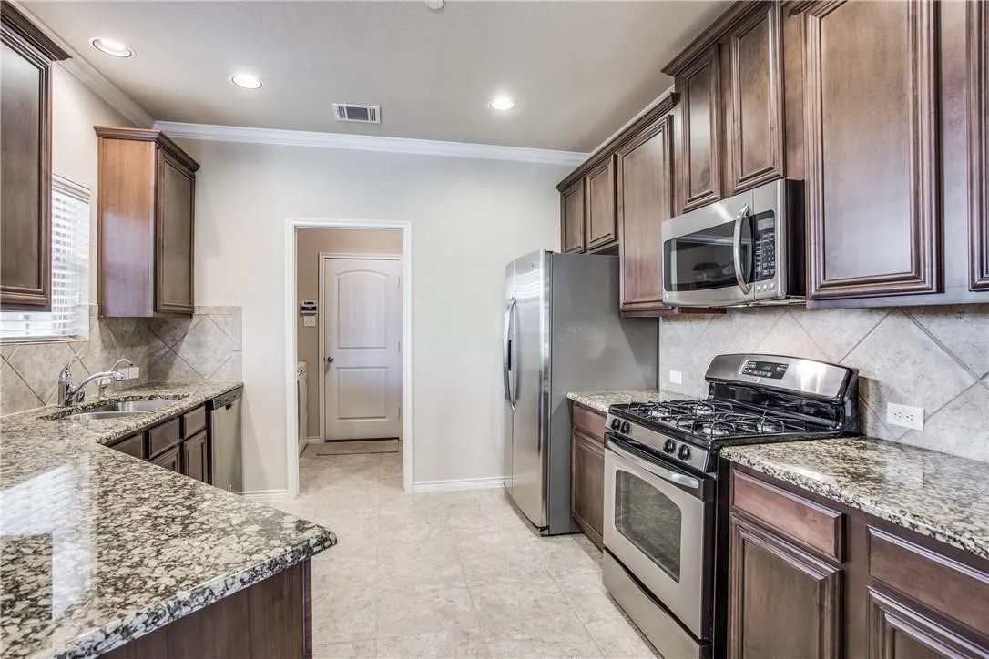 Kitchen featuring granite countertops, stainless steel appliances, dark wood cabinetry, tile flooring, and a tile backsplash