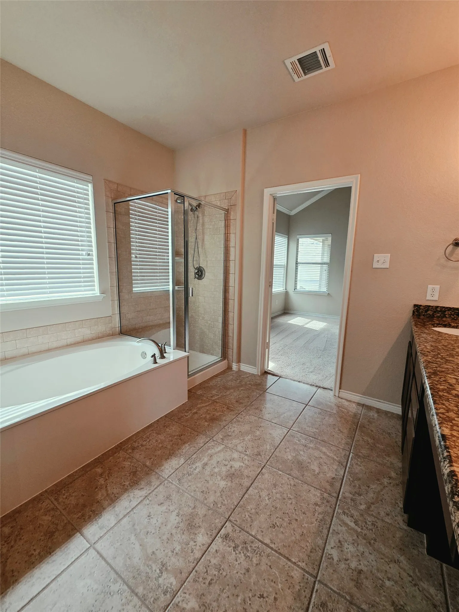 Tiled flooring with a built-in bathtub, a glass-enclosed shower, and a vanity with a stone countertop