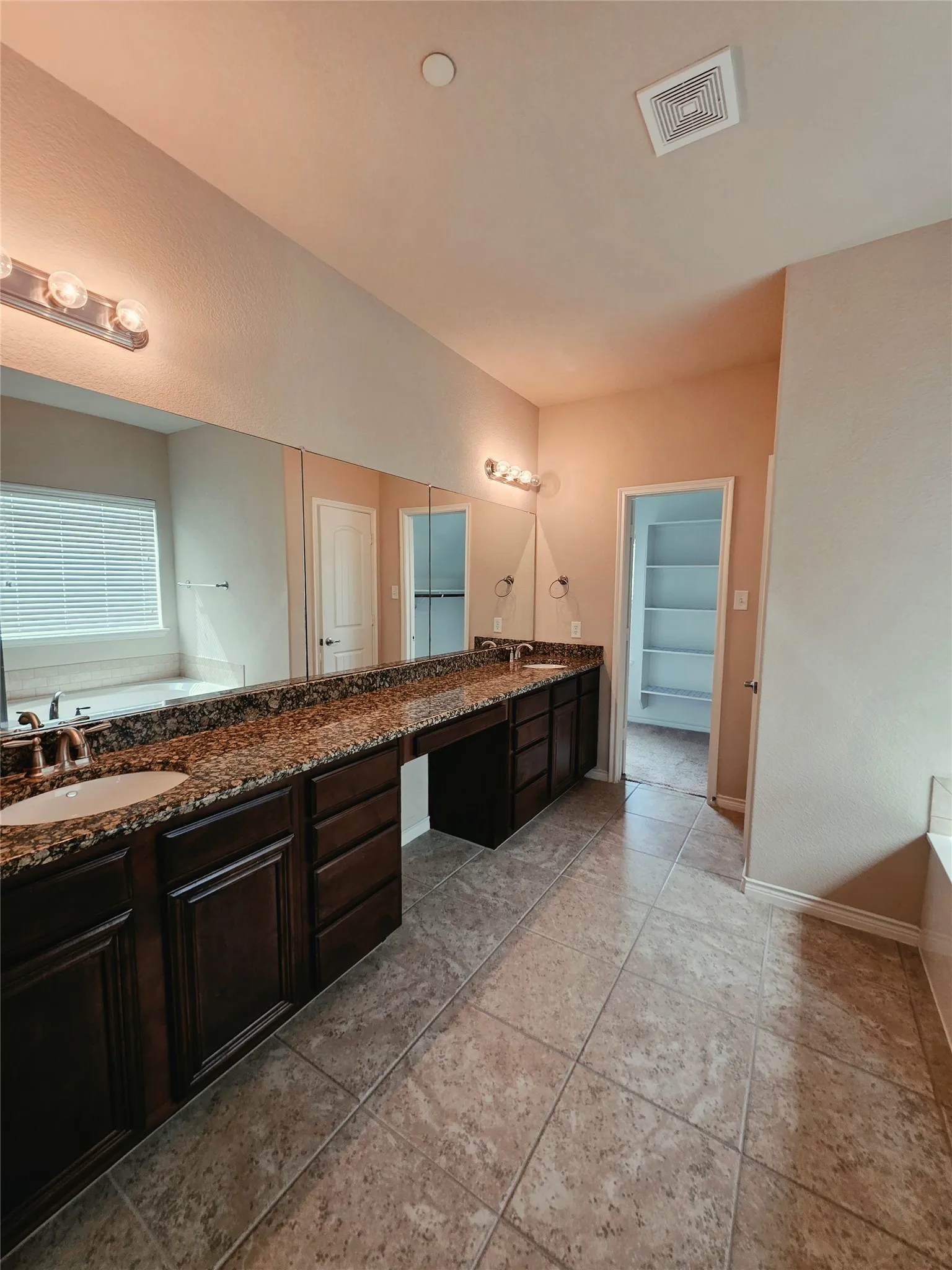 Dual vanity with dark wood-finish cabinetry, speckled countertop, and integrated sinks