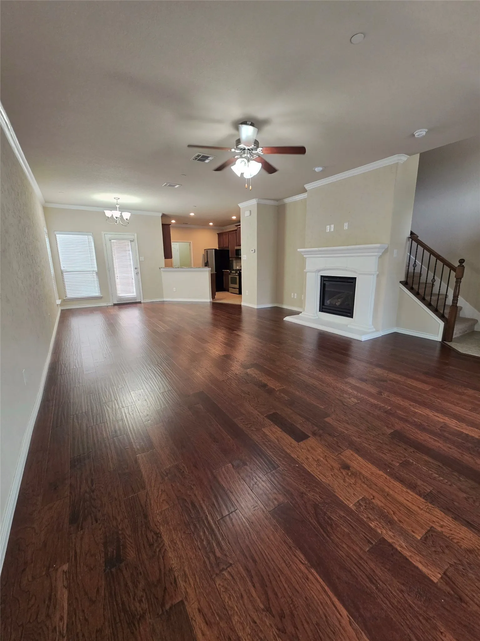 Expansive living area featuring rich wood-finish flooring, a contemporary fireplace with a classic mantel, and a ceiling fan with integrated lighting