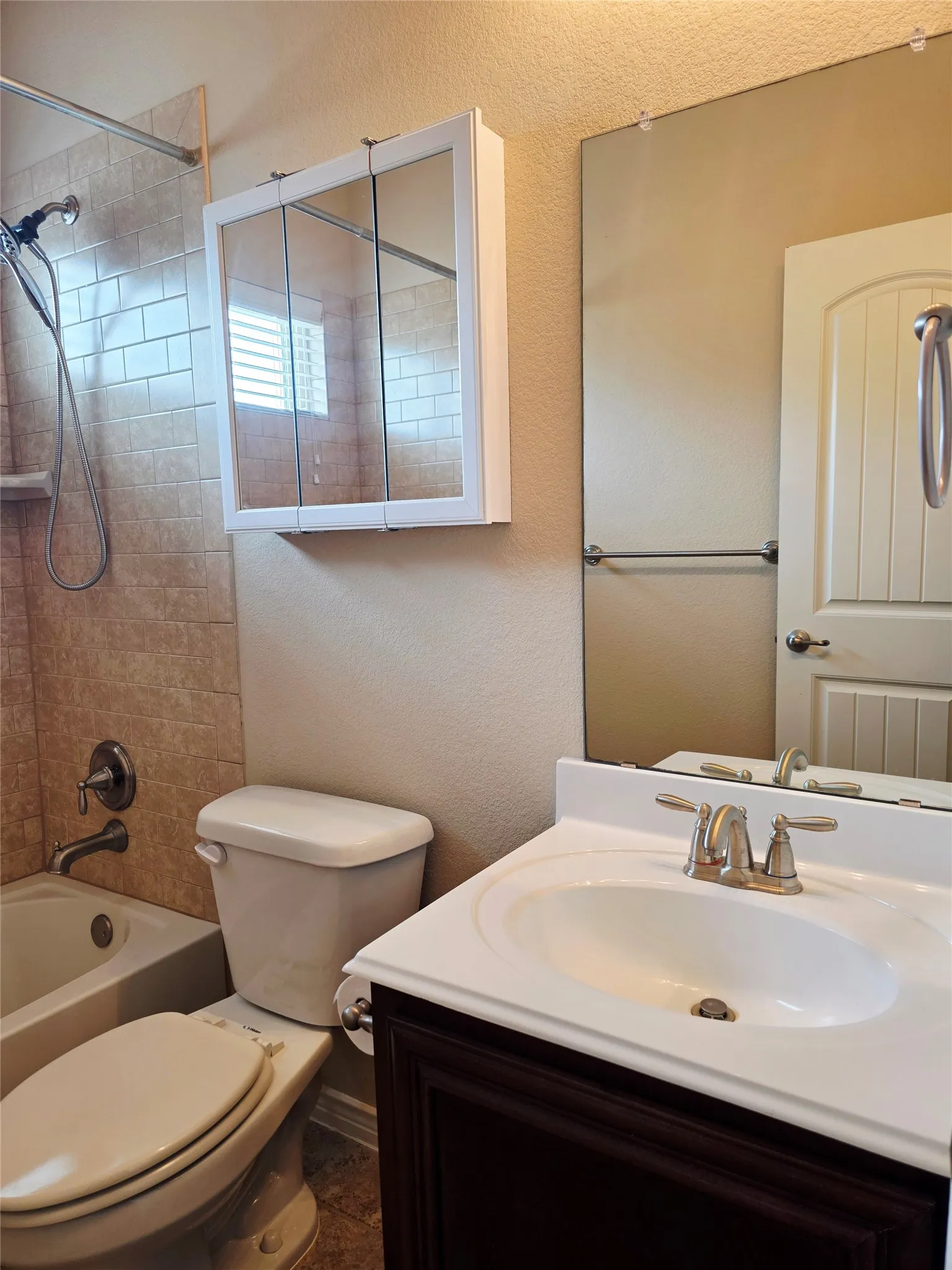 White cabinet with double mirrored doors, vanity with integrated white sink, dark wood-finish vanity cabinet, large wall-mounted mirror, and tiled shower surround