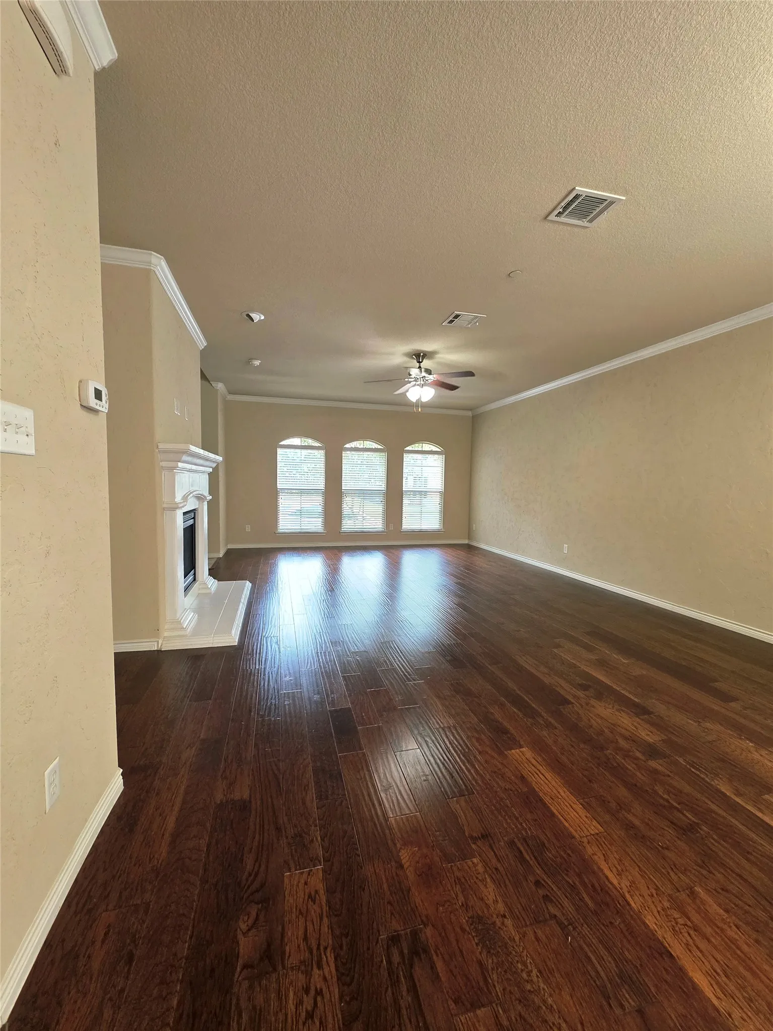 Rich wood-finish flooring, a white mantel fireplace, and three arched windows