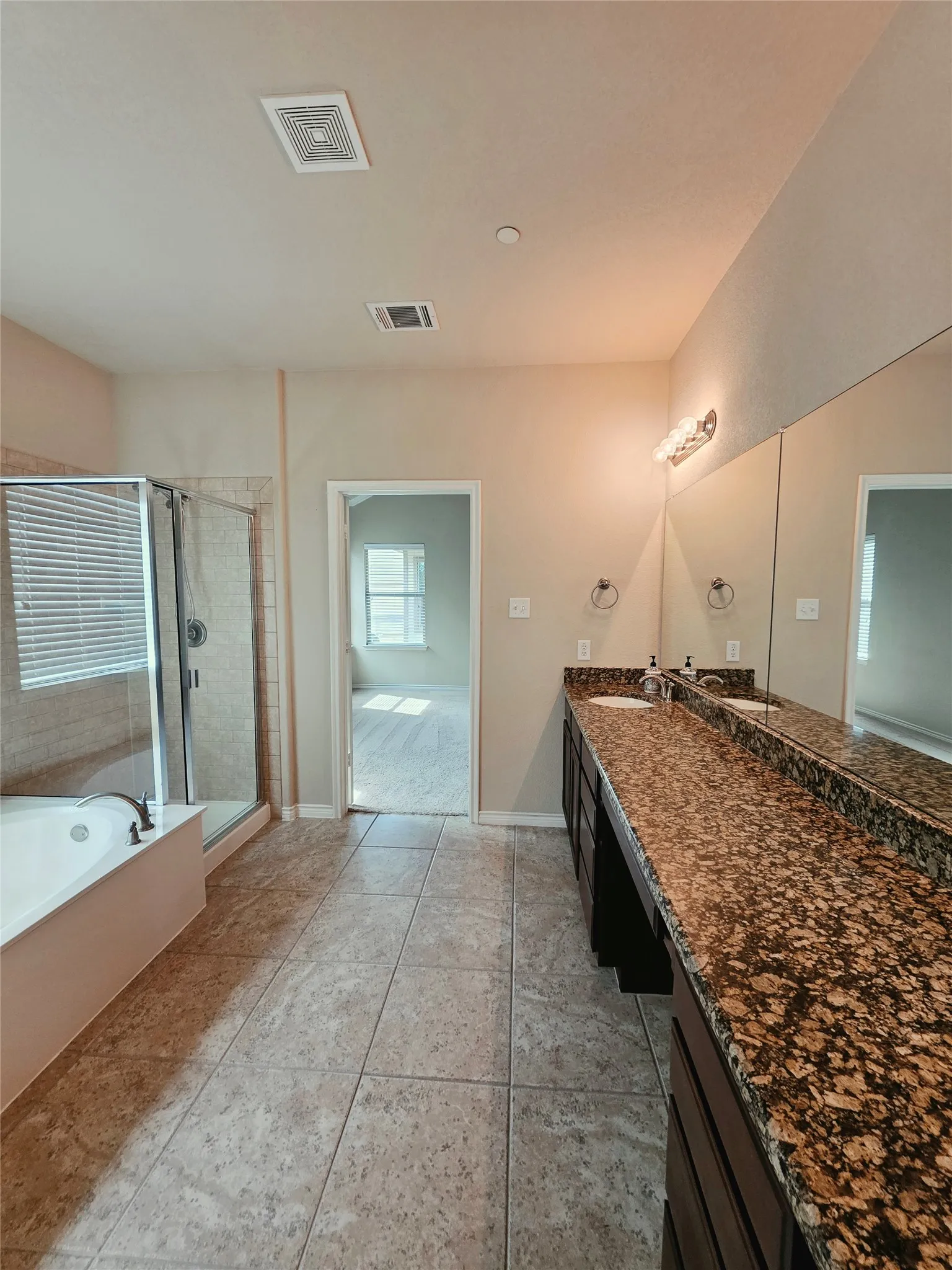 Spacious bathroom featuring a dual vanity with granite countertops, an integrated soaking tub, a glass-enclosed shower, and tile flooring