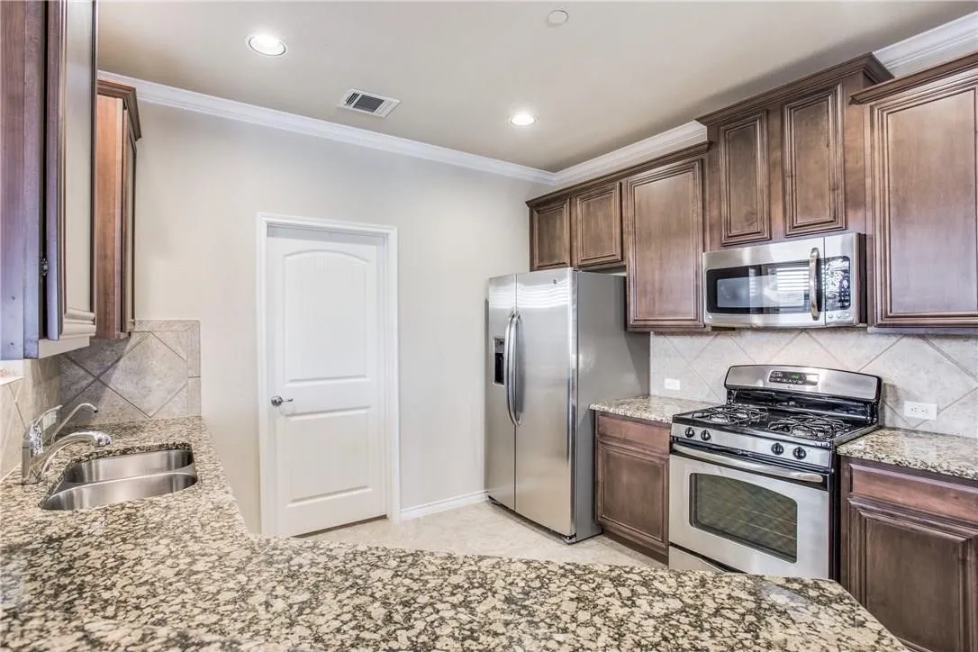 Kitchen featuring granite countertops, stainless steel appliances, dark wood cabinetry, and a tile backsplash