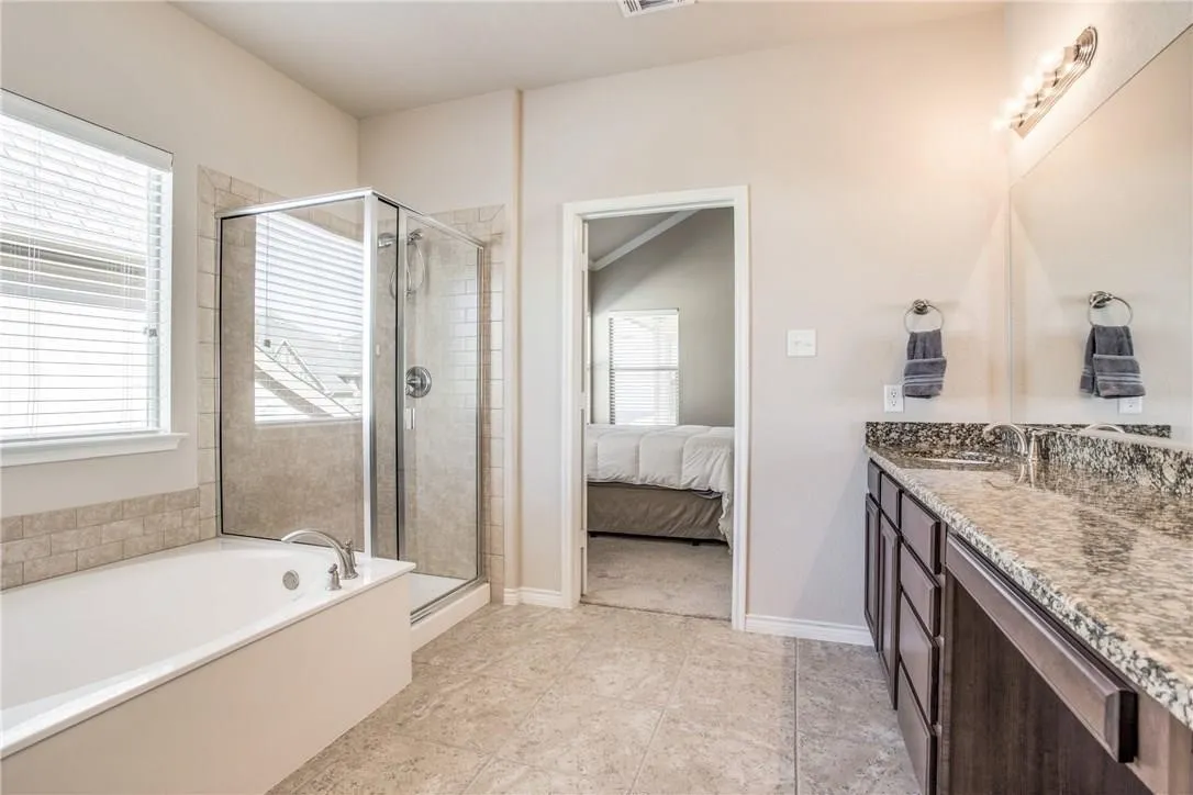 Bathroom featuring a built-in tub, separate glass-enclosed shower, dual vanity with undermount sinks, and a stone countertop