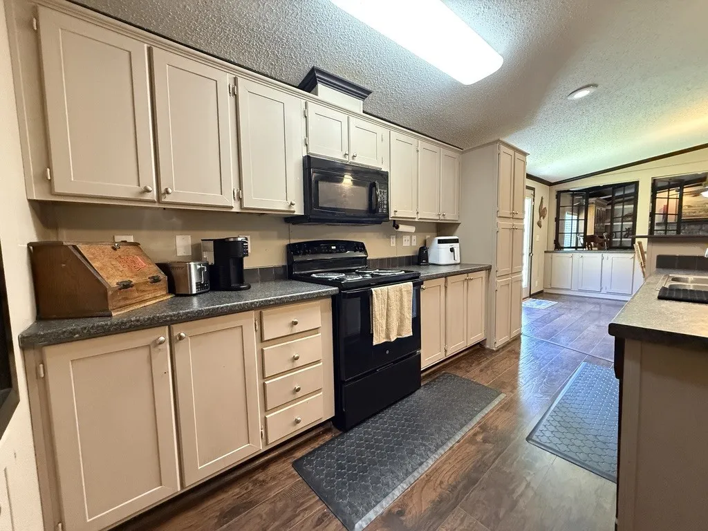 Kitchen featuring extensive cabinetry, dark wood-finish flooring, dark countertops, and a full suite of black appliances including a range and microwave