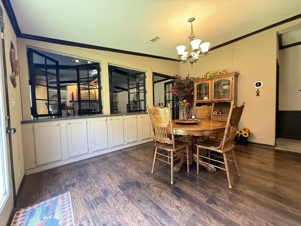 Spacious room featuring wood-finish flooring, a contemporary chandelier, and extensive built-in lower cabinetry with a light-toned countertop