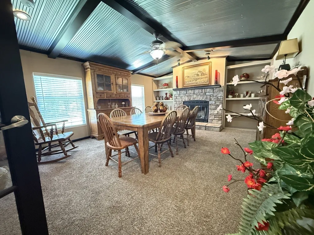 Dining area featuring a stone fireplace with a wood mantel, recessed lighting, and a corrugated metal ceiling with dark wood beams