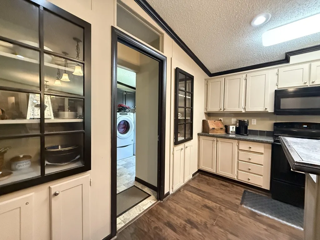Kitchen area featuring wood-finish flooring, light-toned cabinetry, and black appliances