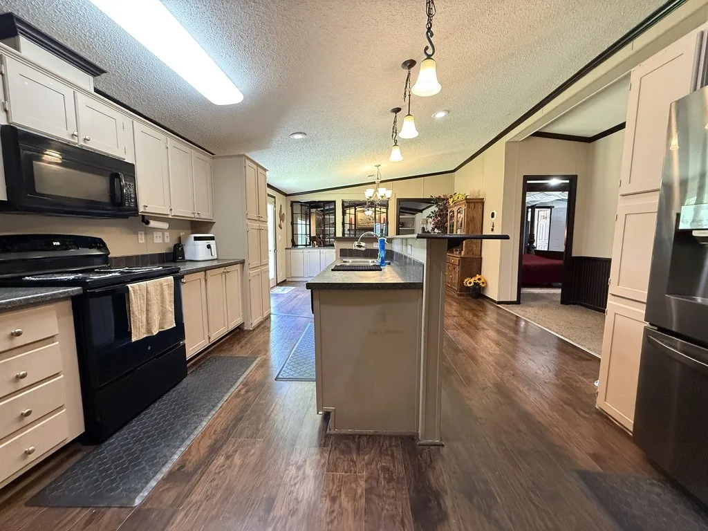 Kitchen featuring wood-finish flooring, light-toned cabinetry, dark countertops, and black appliances