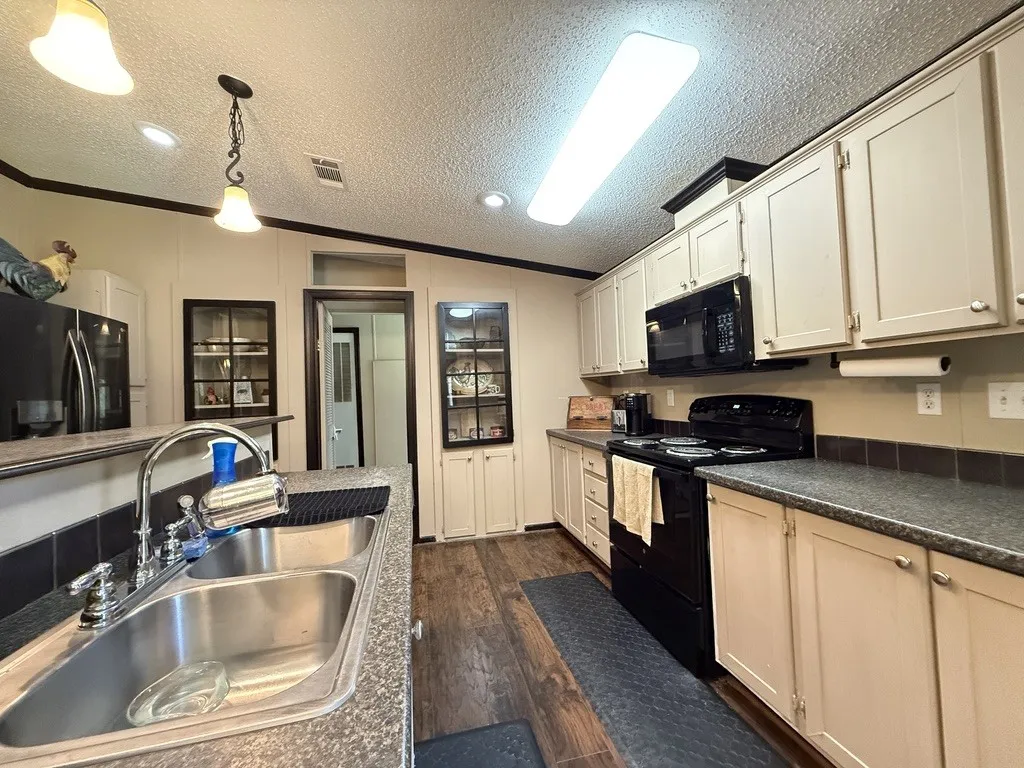 Kitchen featuring dark wood-finish flooring, light-toned cabinetry, dark countertops, a double basin stainless steel sink, and black appliances