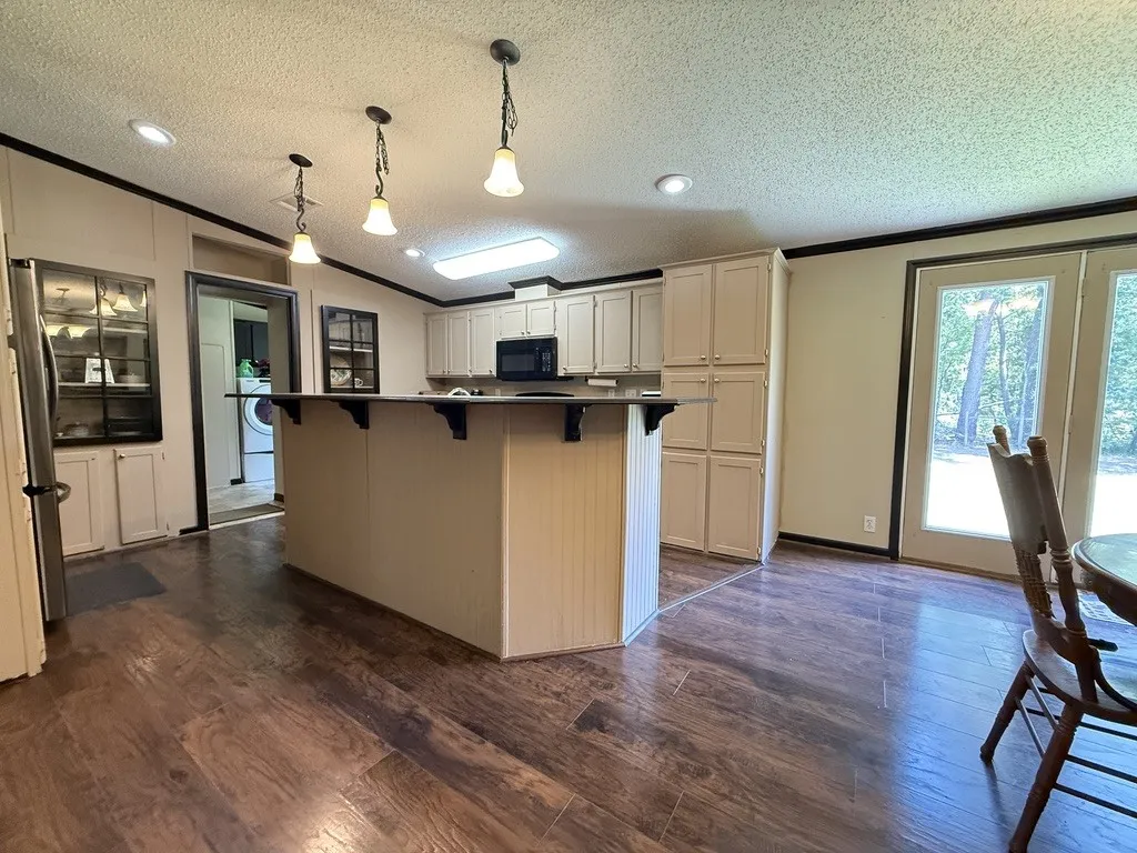 Spacious kitchen featuring a dark-toned island with decorative corbels, wood-finish flooring, white cabinetry with dark hardware, built-in microwave, and recessed lighting