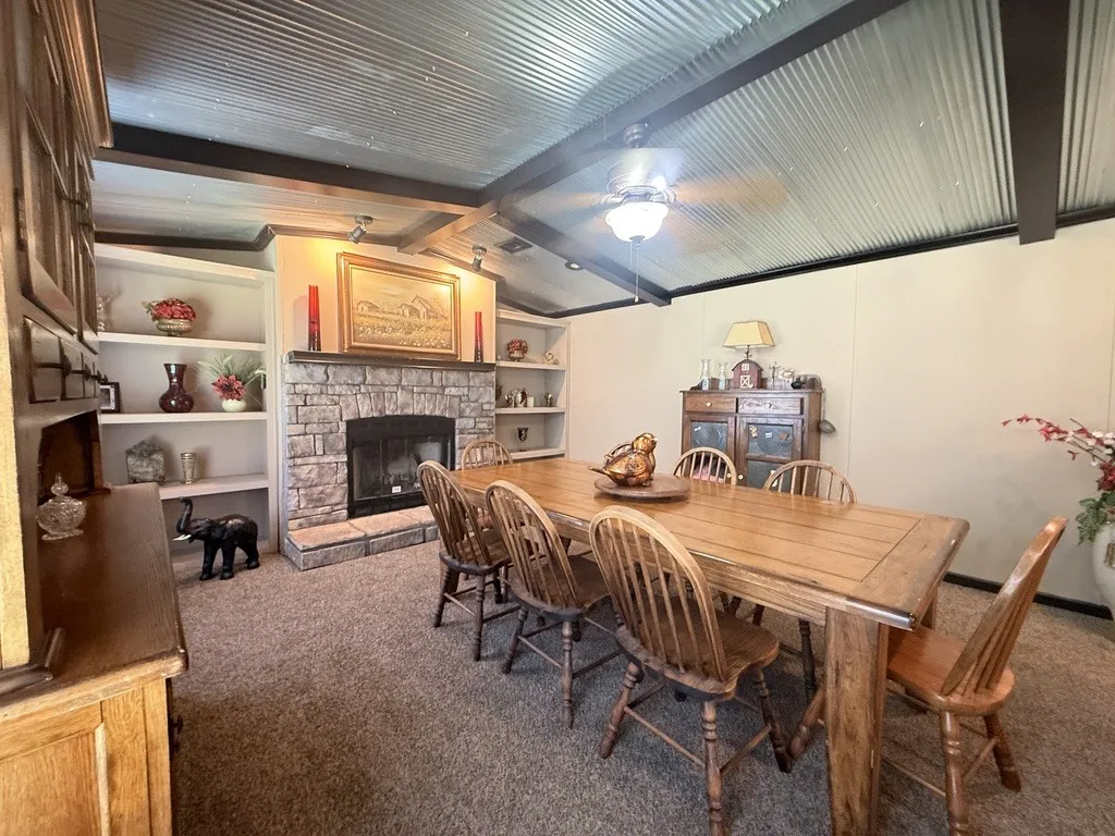 Living area featuring a stone fireplace with a wood mantle, built-in shelving, wood-finish flooring, and a corrugated metal ceiling with exposed beams
