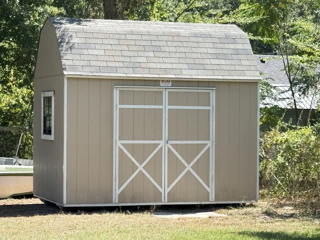 Freestanding storage shed featuring a gambrel roof with asphalt shingles, neutral-toned siding, and double barn-style doors