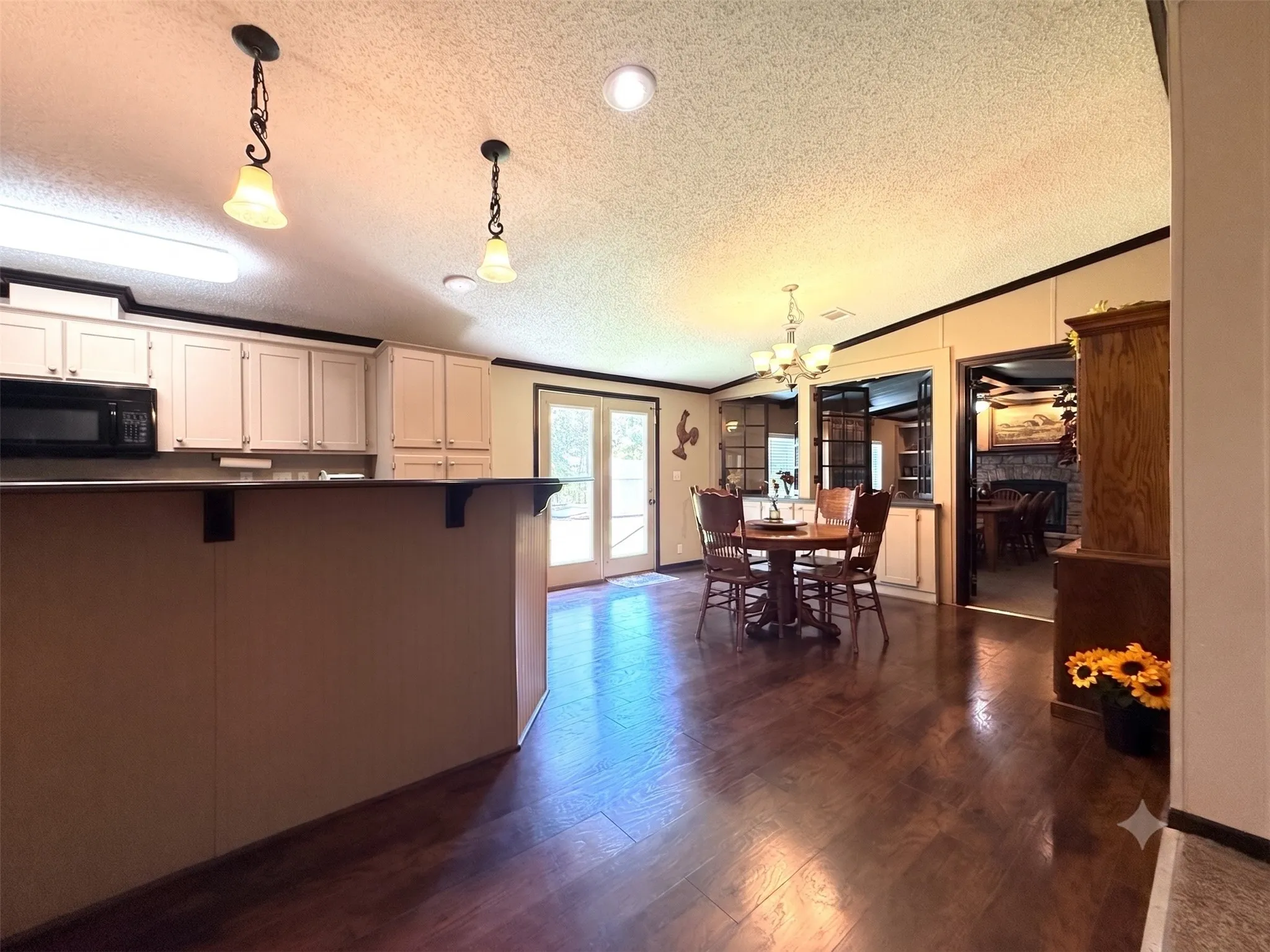 Open-concept kitchen and dining area featuring wood-finish flooring, a kitchen island with a breakfast bar, light-toned cabinetry, and double French doors
