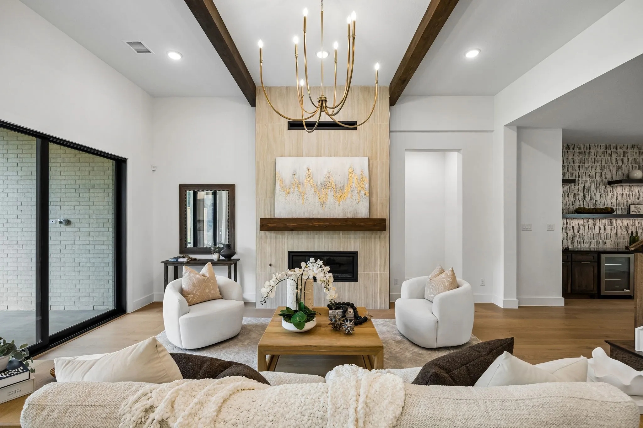 Vaulted ceiling with exposed wood beams, a fireplace with a light-toned surround and wood mantel, large sliding glass doors, and a built-in wet bar with shelving