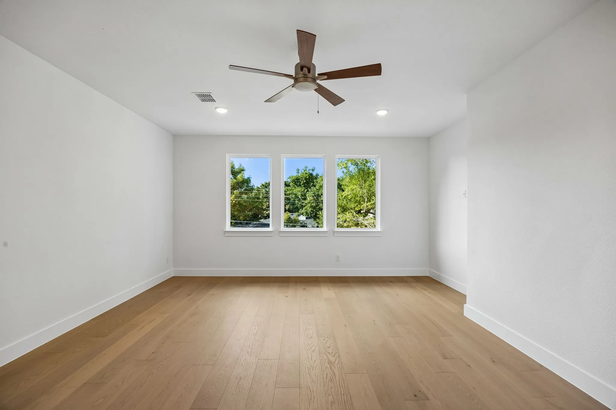 Bright interior with three windows, wood-finish flooring, a ceiling fan, and recessed lighting