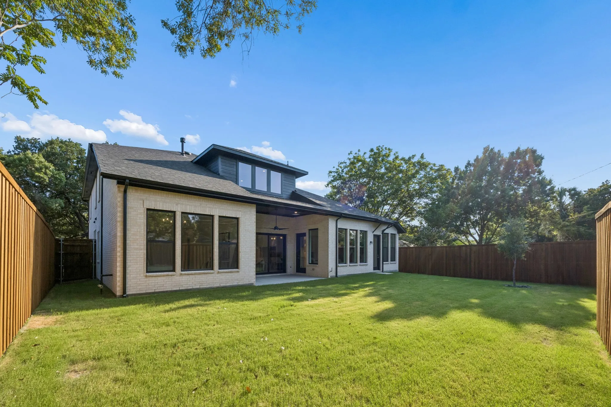 Expansive backyard featuring a manicured lawn, wood privacy fencing, and a brick-clad exterior