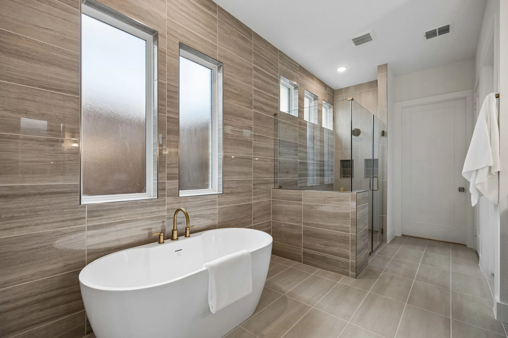 Freestanding soaking tub with brass fixtures, glass-enclosed shower, and full-height tiled walls