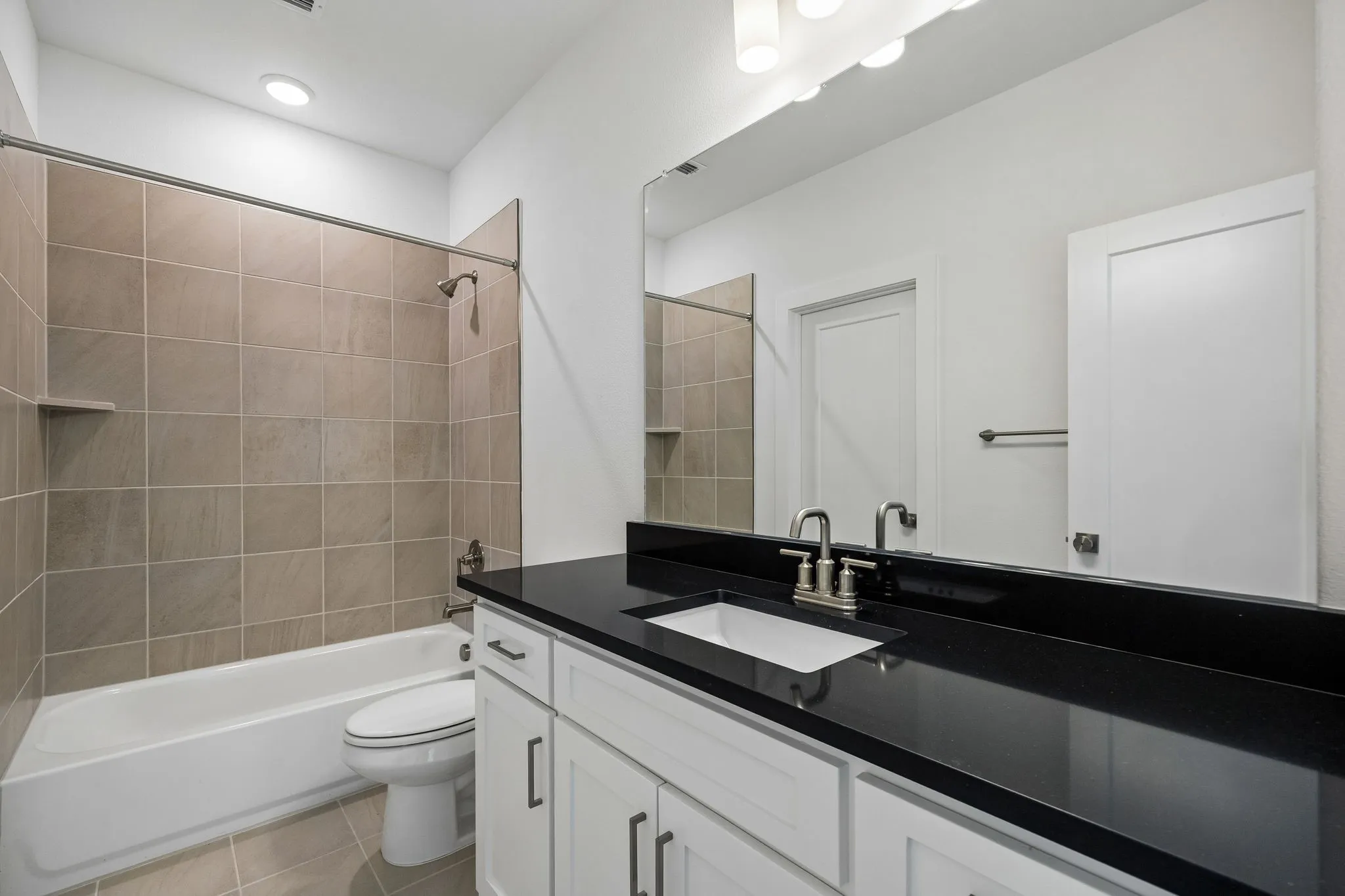 White vanity with dark countertop, large mirror, and tile-surrounded tub with shower