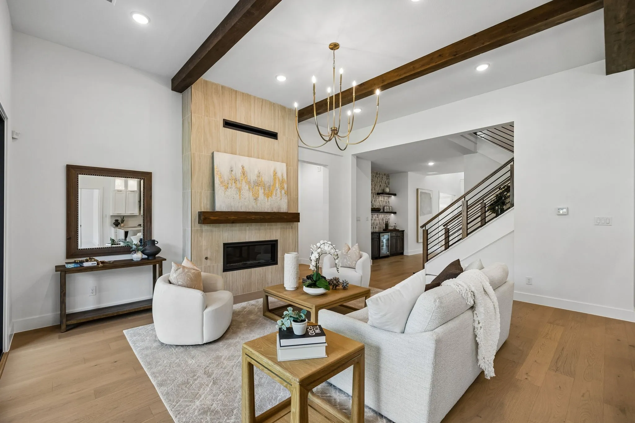 Vaulted ceiling with exposed wood beams, wood-finish flooring, built-in fireplace with a tiled surround, chandelier lighting, and a modern stair railing