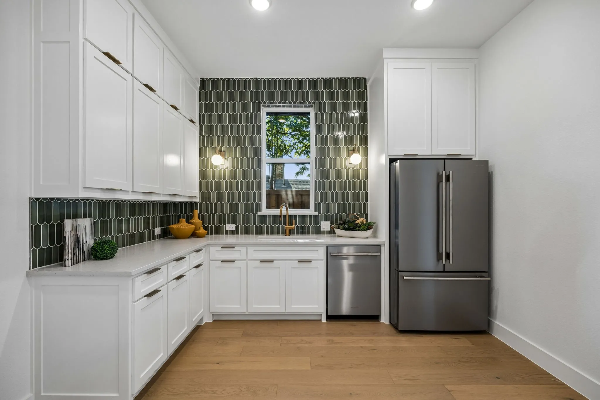 Modern Prep kitchen featuring crisp white cabinetry, stainless steel appliances including a French-door refrigerator, geometric tile backsplash, quartz countertops, recessed lighting, and warm wood-finish flooring throughout the open layout