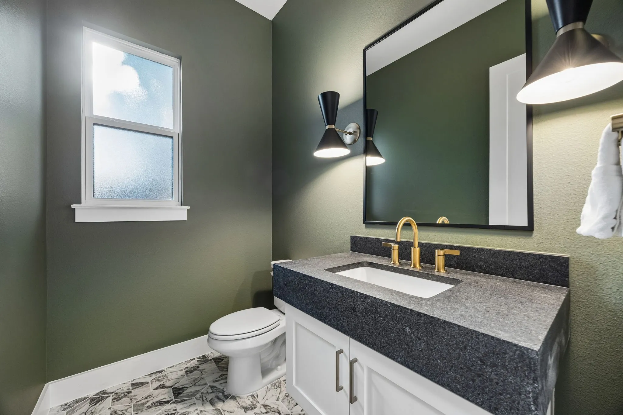 Vanity with a dark stone countertop, undermount sink, and brass-finish faucet