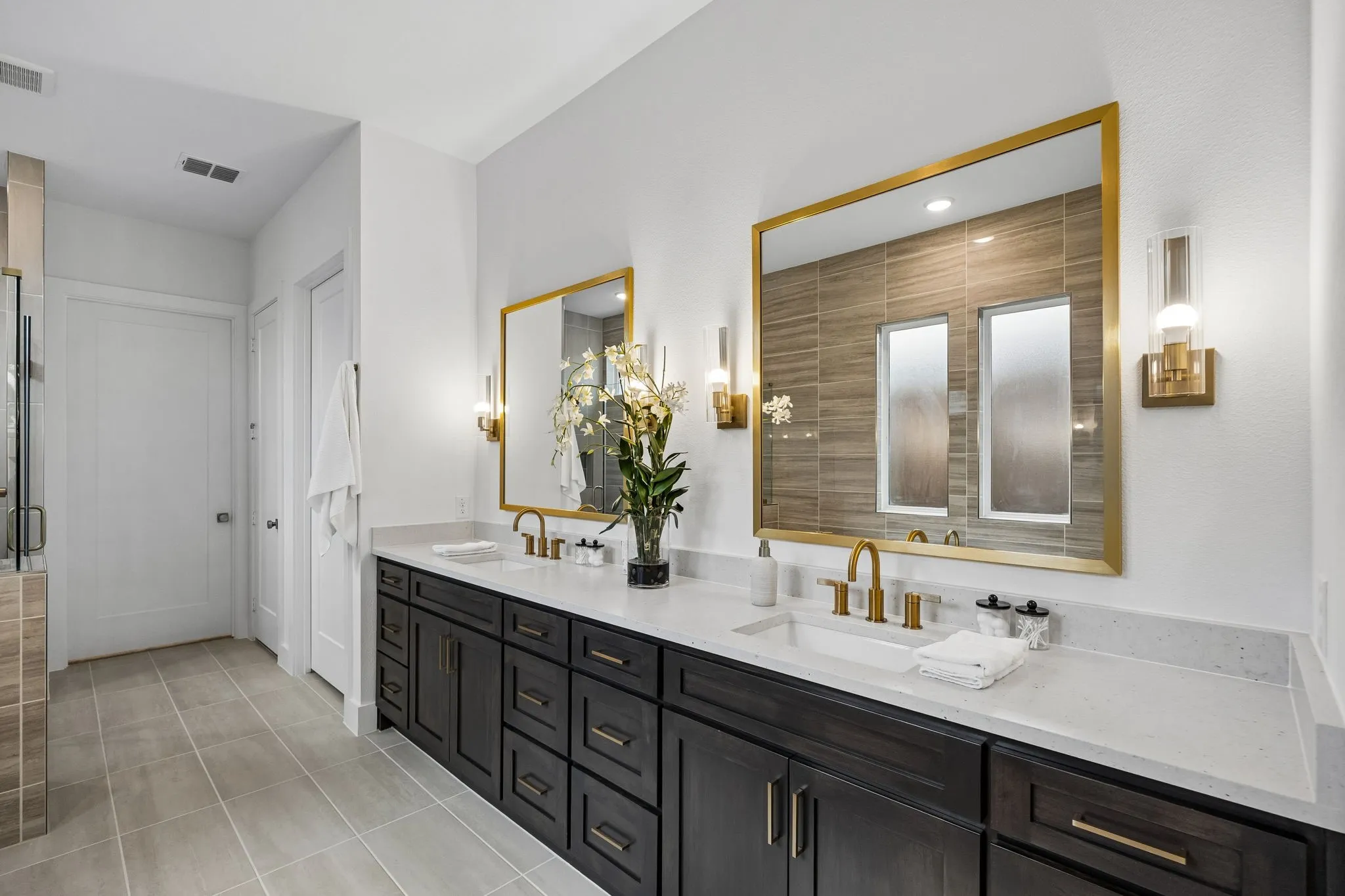 Dual vanity with dark wood-finish cabinetry, white countertops, and gold-finish fixtures