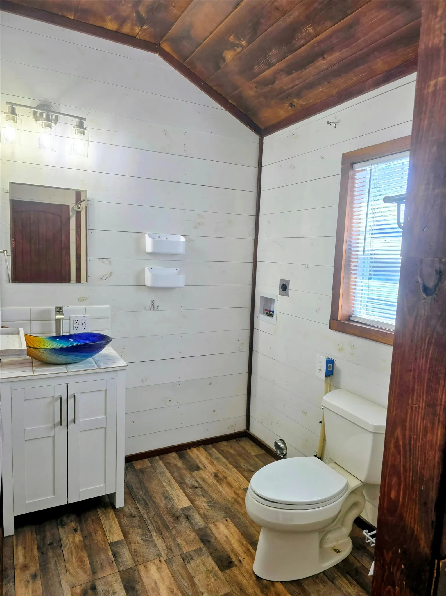 Bathroom featuring wood-finish flooring, white shiplap walls, and a vaulted wood-paneled ceiling