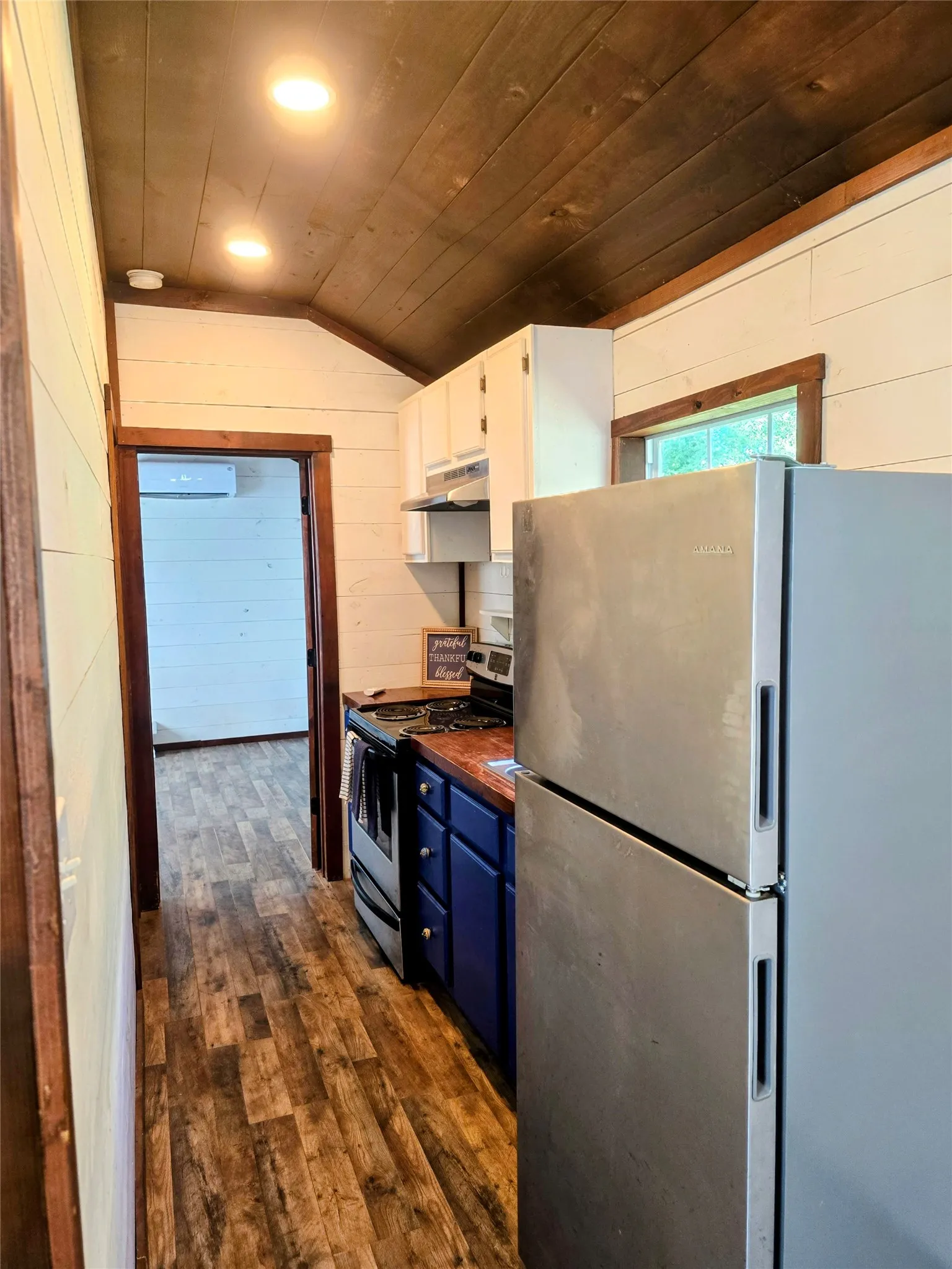 Compact kitchen featuring wood-finish flooring, white shiplap walls, a vaulted wood-paneled ceiling, white upper cabinetry, and blue lower cabinetry