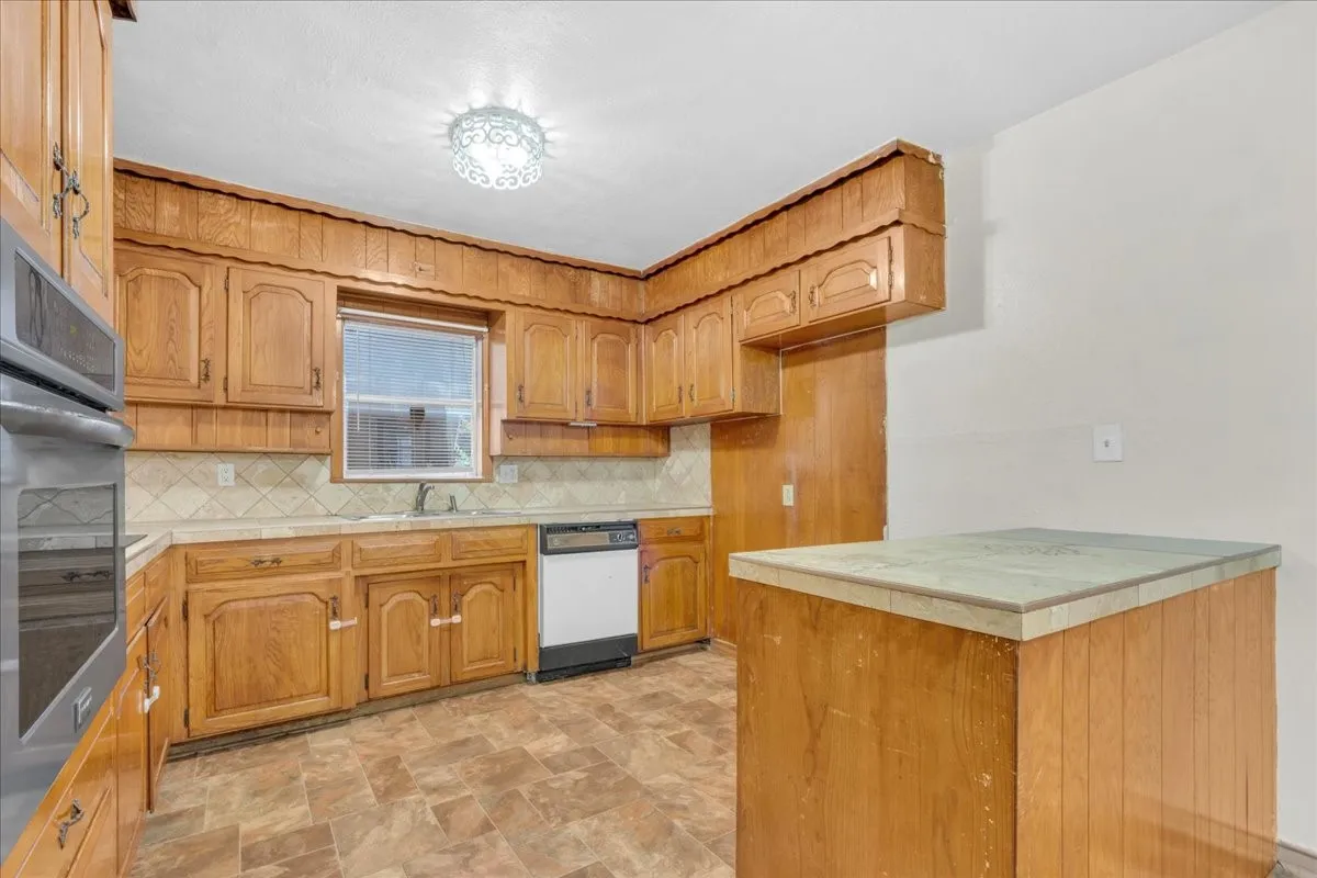 Kitchen featuring wood cabinetry, a built-in oven and microwave, a dishwasher, and a window above the sink