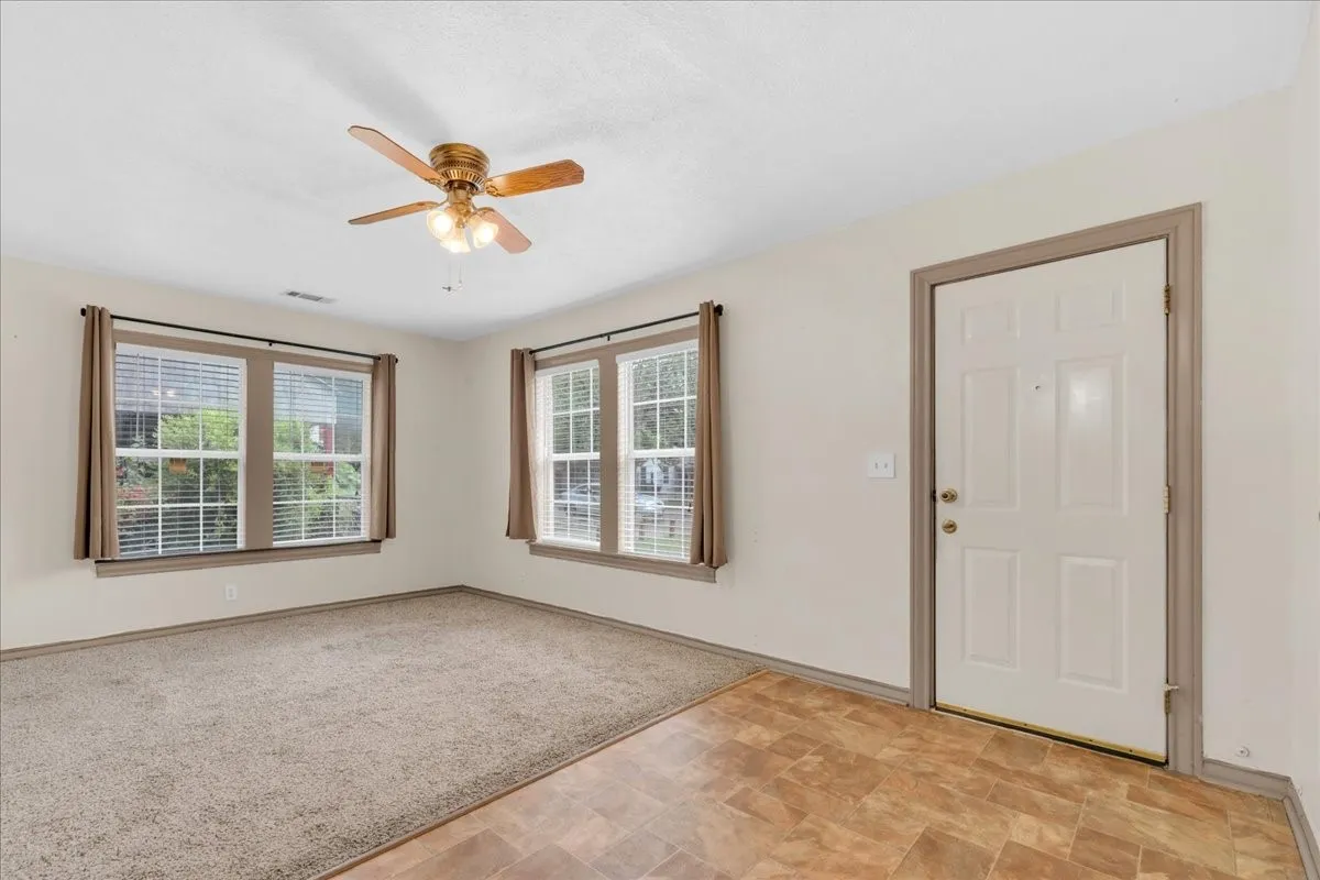 Living area featuring a ceiling fan with integrated lighting, two windows with blinds and curtain rods, and neutral-toned wall-to-wall carpeting