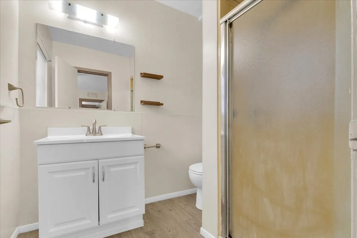 Bathroom featuring a single vanity with a white cabinet, a wall-mounted mirror, a two-bulb vanity light, and light wood-finish flooring