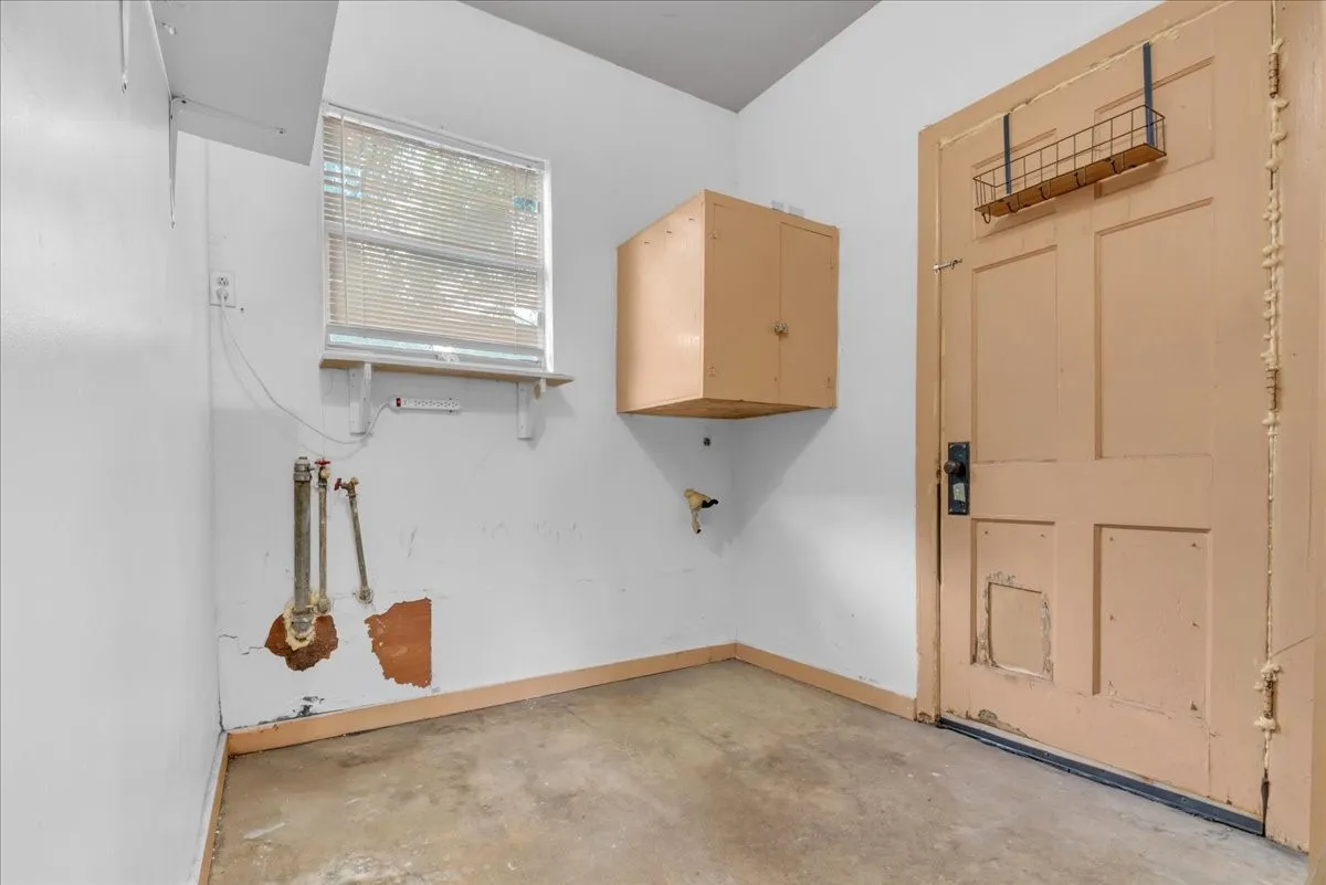 Utility room featuring a window with blinds, wall-mounted cabinetry, and exposed plumbing hookups