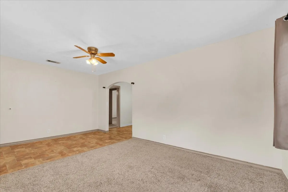 Spacious interior room featuring a ceiling fan with integrated lighting, a broad arched doorway, and a combination of neutral-toned carpeting and wood-finish flooring