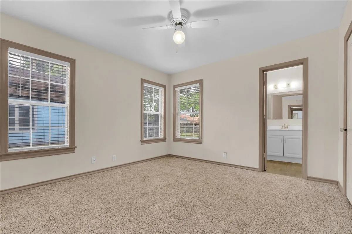 Carpeted room featuring multiple windows with blinds, a ceiling fan with light fixture, and neutral wall paint